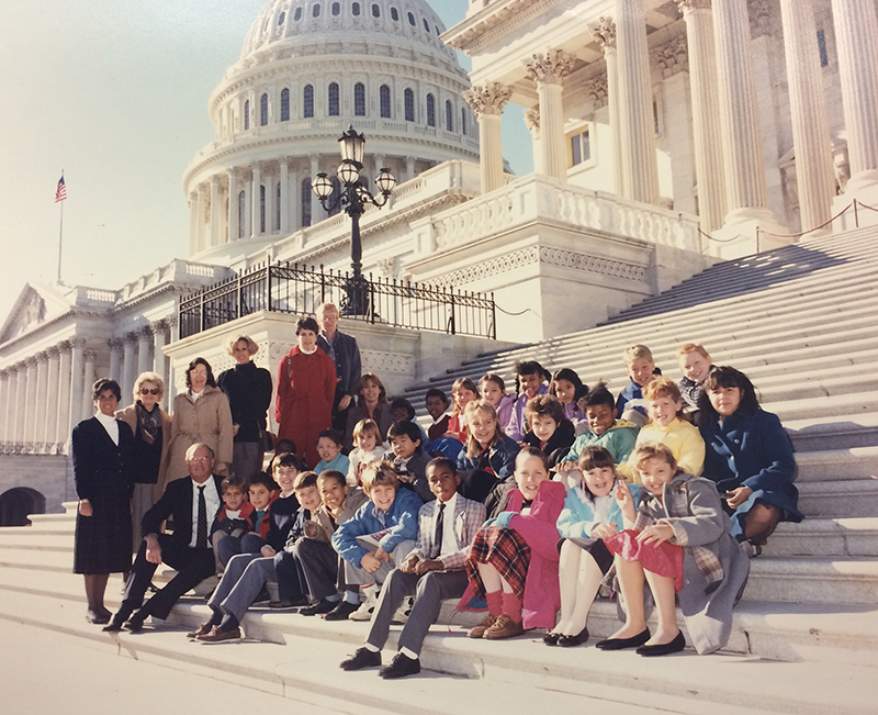 Color photograph of Washington Mill students on a field trip to Washington, D.C. There are approximately 27 students seated on the steps of the U.S. Capitol building. Eight unidentified adults are pictured with them. 
