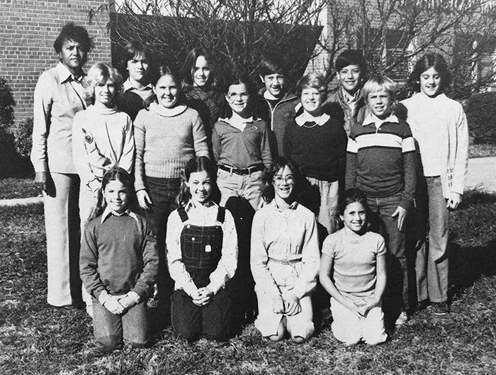 Black and white yearbook photograph of Washington Mill's SCA taken in 1981 or 1982. 14 children and a teacher are pictured. They are posed in front of a cherry tree near our main entrance. The tree is not yet in bloom and is much smaller than it is today. 